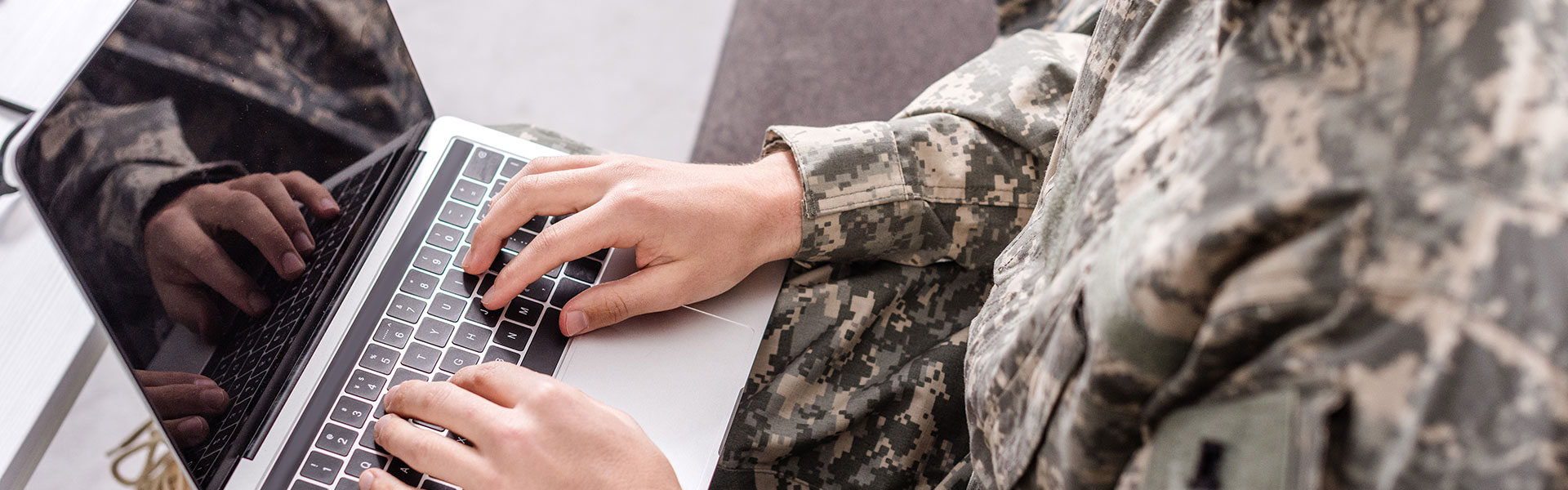 A person in military fatigues typing on a laptop.